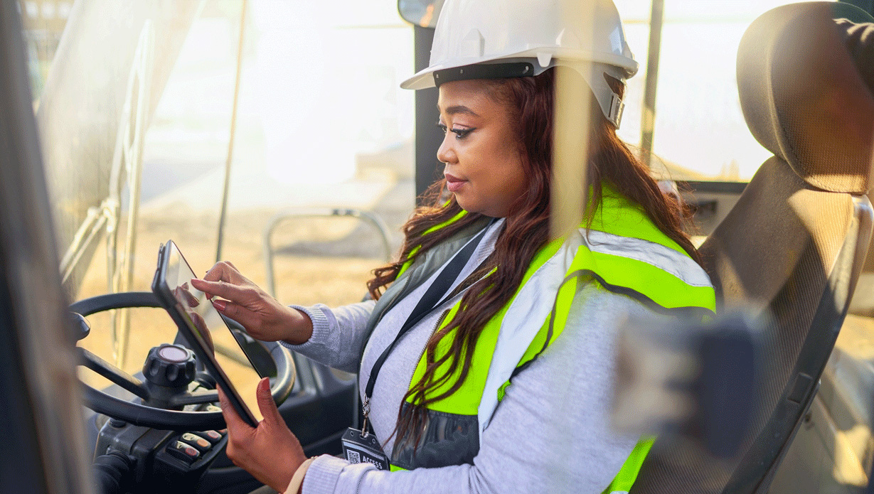 Vrouw met witte helm en veiligheidshesje bestuurt een vorkheftruck